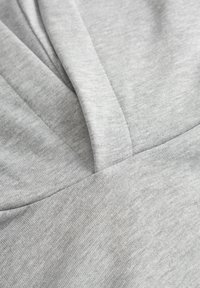 Hellgrauer Stoff mit glatter Textur, der ein gefaltetetes Design und Nähte zeigt und ein weiches, lässiges Aussehen präsentiert.