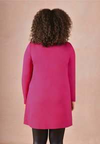 Fuchsiové šaty s dlouhým rukávem, rovného střihu, s texturovanou tkaninou a hladkým povrchem, dosahující do poloviny stehna, nošené přes černé legíny.