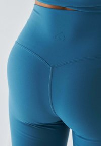 Legginsy z wysokim stanem w kolorze morskim, wykonane z elastycznego materiału, o gładkiej fakturze i małym logo w kształcie serca wytłoczonym na pasie.