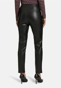 Pantalones de imitación cuero negros con un ajuste slim, cintura alta y dos bolsillos traseros. La textura es suave y se combinan con tacones negros puntiagudos.