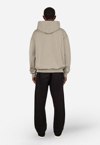 Bluza z kapturem w jasnoszarym kolorze, wykonana z miękkiego materiału. Luźny krój z prążkowanymi mankietami i dołem, zestawiona z czarnymi luźnymi spodniami.