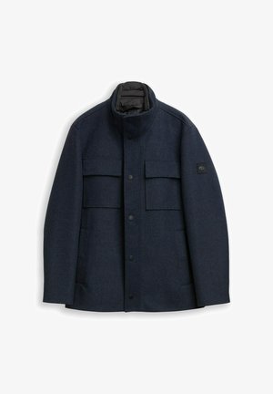 Navy blue coat made from textured fabric, featuring a high collar, buttoned front, and two chest pockets with a logo patch on the sleeve.