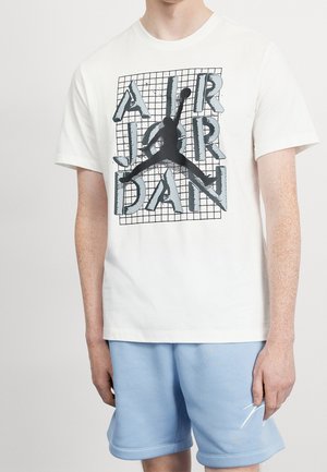 Biała bawełniana koszulka z grafiką czarnego sylwetki oraz napisem "AIR JORDAN" w niebieskim i szarym kolorze na tle wzoru siatki.