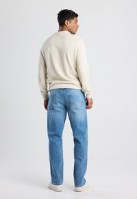 Pullover beige chiaro con scollo rotondo, abbinato a jeans in denim azzurro. L'outfit ha una vestibilità rilassata e una texture morbida.