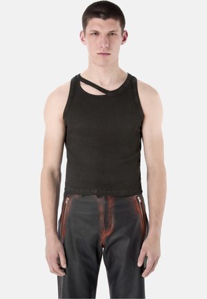 Young man wearing a black sleeveless top with a diagonal cutout near the neckline and black leather pants with orange accents and zipper pockets.