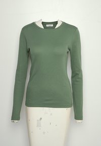 Pitkähihaisessa vihreässä paidassa on ribbikangas ja kontrastivalkoinen yksityiskohta pääntiellä.