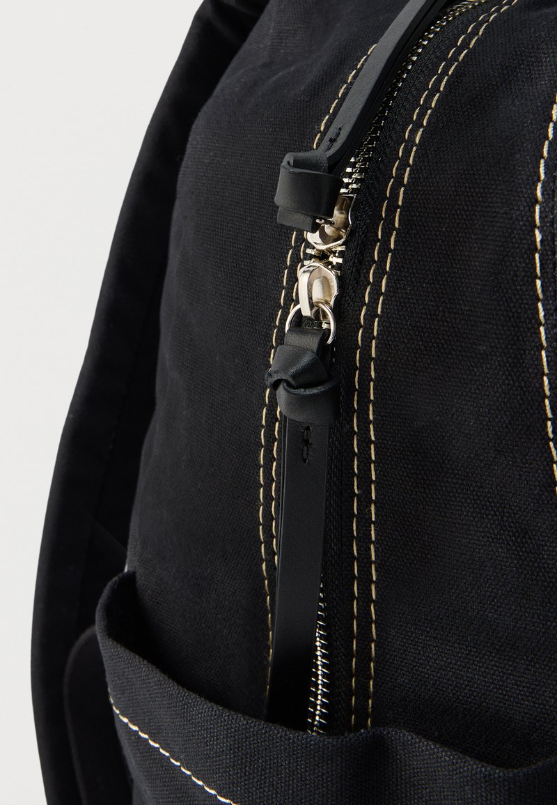 Sort stofpose med beige kontrastsyning og sølvlynlås med sort lædertræk med knudedetalje.