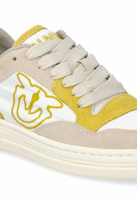 Beige suede and white leather sneaker with yellow accents and stitching. Features laces and a graphic design on the side. Textured sole.