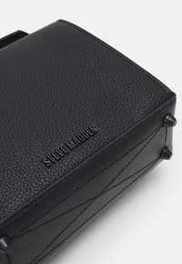 Coin de sac en cuir noir texturé avec quatre pieds métalliques protecteurs et nom de marque embossé "STEVE MADDEN".