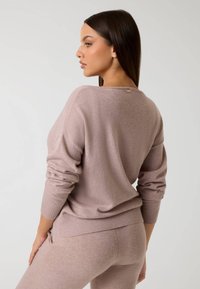 Suéter de punto rosa claro con un ajuste relajado, que presenta puños y dobladillo acanalados, y una pequeña etiqueta de marca en el cuello trasero. Textura suave.
