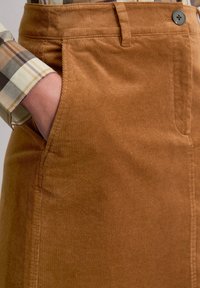 Bruine corduroy rok met een gladde textuur, verticale ribbels en zijzakken. Afgewerkt met een decoratieve zwarte knoop op de tailleband.