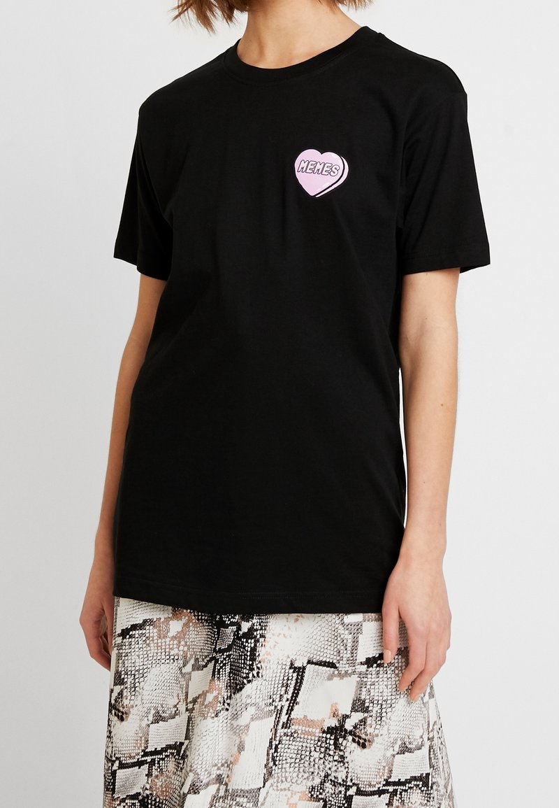 Czarna bawełniana koszulka z krótkim rękawem, z różowym graficznym sercem z napisem "MEMES" na lewej klatce piersiowej. Klasyczny krój.