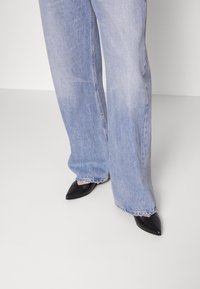 Jasnoniebieskie dżinsy o szerokich nogawkach z denimu, z postrzępionym dołem, w zestawieniu z czarnymi, spiczastymi butami na obcasie, podkreślające gładką fakturę.