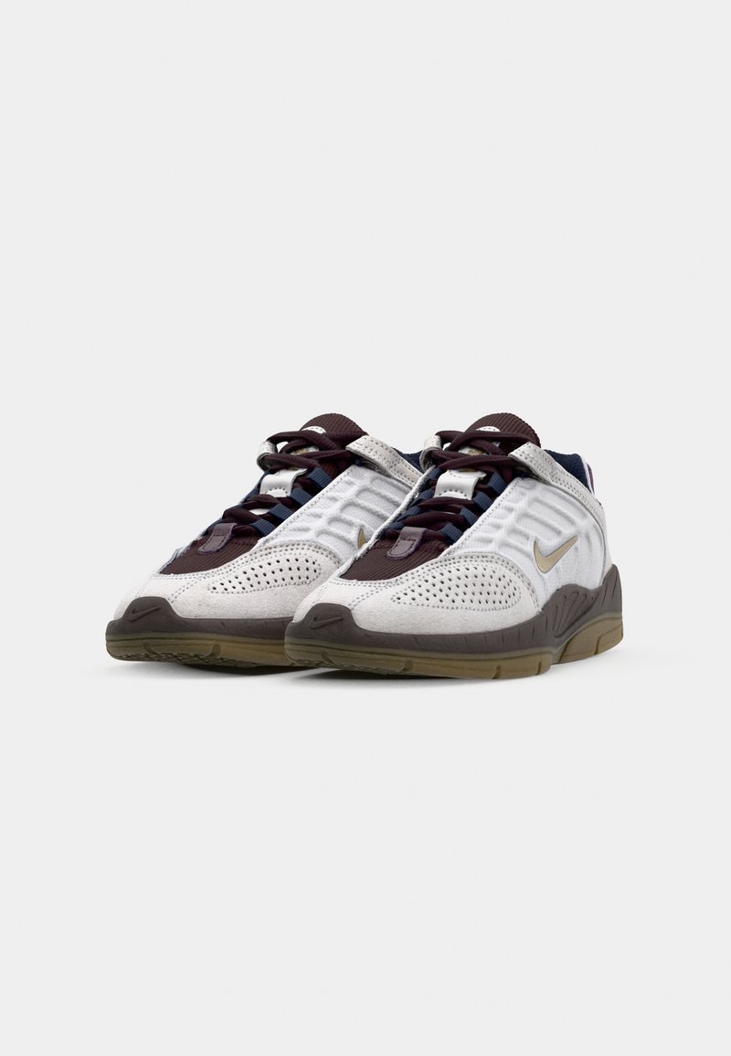 Baskets de sport blanches et grises avec un tissu texturé, des accents violets, des sections perforées et une semelle en caoutchouc marron. Logo Nike présent.