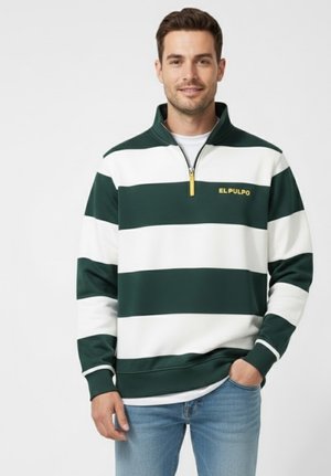 Hombre vistiendo un sudadera de media cremallera de rayas anchas en verde y blanco con el texto "EL PULPO", combinada con jeans de color azul claro, de pie frente a un fondo blanco.