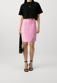 Camiseta negra corta, falda ajustada rosa, sandalias negras de tacón alto, sosteniendo un bolso negro. Diseño sencillo, texturas de tela suaves.