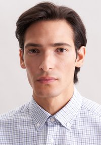 Camicia con colletto a motivi a scacchi blu e bianchi. Tessuto morbido, design con bottoni e texture liscia. Sfondo neutro, inquadratura ravvicinata.