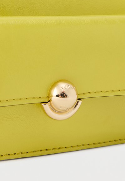 Rabatt en cuir vert citron avec fermoir circulaire en or gravé "FURLA" et couture visible le long des bords.