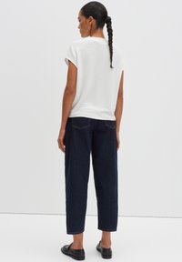 Haut blanc à manches courtes en tissu léger, associé à un pantalon large en denim bleu foncé, présentant un design simple de poche à l'arrière.