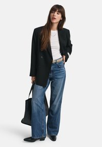 Zwarte dubbel gevallen blazer, witte t-shirt, high-waisted blauwe spijkerbroek met flared pijpen, zwarte handtas en zwarte puntige enkelbooties.