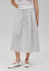 White tiered skirt with black polka dots, made of lightweight fabric. Paired with light-colored flat shoes featuring a small strap detail.