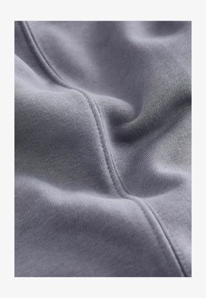 Grau gefärbter Stoff mit glatter Textur weist eine sichtbare Naht und eine leichte Dehnbarkeit auf, die für verschiedene Anwendungen wie Bekleidung oder Polsterung geeignet ist.