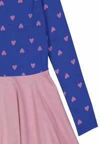 Blauwe top met lange mouwen en roze hartpatronen, gecombineerd met een roze uitlopende rok. Zachte stof met een ribbelstructuur op de top.