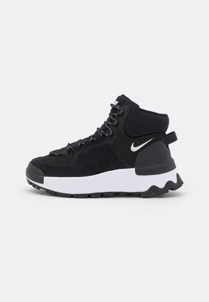 Czarno-białe wysokie tenisówki Nike z teksturowaną podeszwą, wiązane z przodu i z wyściełanym kołnierzem wokół kostki na jednolitym tle.