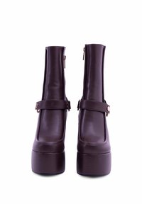 Stivaletti alla caviglia in finta pelle marrone con punta quadrata, chiusura con zip e una larga fascia sopra la caviglia. Suola spessa e piattaforma.