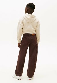 Beige hoodie with a drawstring, paired with wide-leg, dark burgundy corduroy pants. White sneakers with red and blue accents.