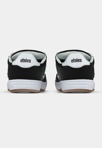 Ζευγάρι μαύρων και άσπρων χαμηλών παπουτσιών Etnies, εμφανιζόμενο από πίσω σε λευκό φόντο.