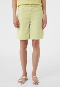 Jasnożółte szorty dżinsowe o prostym kroju, pięciokomorowym designie i zapięciu na guzik. Połączone z białymi sandałami na płaskiej podeszwie z paskami.