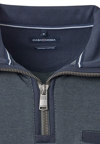 Camicetta blu con zip colletto realizzata in cotone di alta qualità, caratterizzata da una superficie testurizzata, zip argentata e strisce bianche vicino al collo.