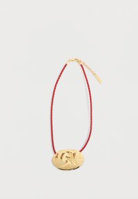 Złoty owalny wisiorek z misternie wyciętym wzorem, przymocowany do plecionej czerwonej naszyjnika z złotym zapięciem i łańcuszkiem przedłużającym.