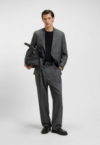 Completo grigio a quadri con giacca aderente e pantaloni plissettati, abbinato a una maglietta nera, cintura di pelle e borsa a mano in pelle nera.