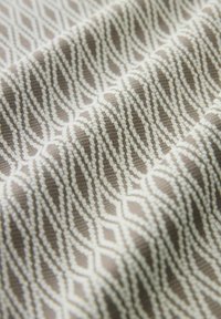 Tissu texturé beige et blanc avec un motif géométrique répétitif de diamants et d'ovales, présent dans des plis doux.