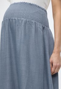 Φούστα ανοιχτού γαλάζιου χρώματος με ελαστική μέση και ρέον ύφασμα. Η υφή είναι απαλή, δημιουργώντας απαλά πτυχώσεις και ένα χαλαρό σιλουέτα.