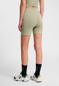 Höga olivgröna shorts med en texturerad yta, med sidodetaljer och en figurnära design, kombinerade med svarta strumpor och sportskor.