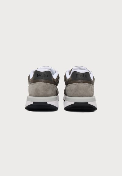 Ζευγάρι χαμηλά sneakers με γκρι τακούνια από σουέντ, λευκές επενδεδυμένες περιμετρικές γλώσσες και ασπρόμαυρες σόλες, εμφανιζόμενα από πίσω σε λευκό φόντο.