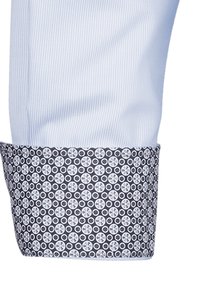 Polsino di una camicia a righe blu chiaro con un accento scuro a motivo, caratterizzato da disegni circolari bianchi su uno sfondo blu navy.