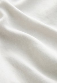 Textured white fabric with a soft, flowing appearance, featuring a fine weave and subtle sheen, capturing light in a gentle manner.