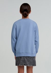 Sweater bleu deschis cu guler rotund și mâneci lungi, asortat cu o fustă din denim închis. Textură moale, croială lejeră, fără modele vizibile.