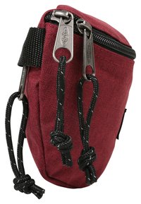 Funda de tela roja con una superficie texturada, con cremalleras y cuerdas negras con nudos; forma compacta y redondeada diseñada para el almacenamiento.