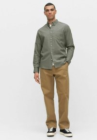 Groene button-up shirt met een zak, gecombineerd met tan rechte broek en zwarte sportschoenen. Soepele textuur, casual pasvorm.