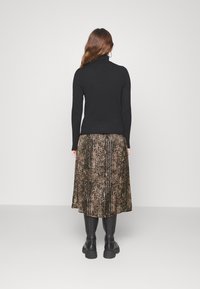 Svart polotröja som matchas med en plisserad kjol i djurmotiv i bruna och gyllene nyanser. Modellen bär svarta knähöga stövlar.