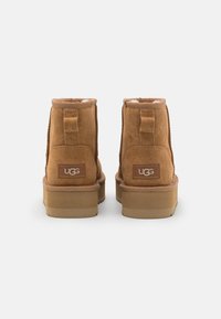 Bottines en suède marron avec une doublure douce, des bouts ronds et une semelle plate. L'arrière présente un patch de marque et une languette pour un enfilage facile.