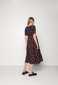 Vestido preto com estampado floral, apresentação de mangas curtas, cintura ajustada e uma saia midi rodada com padrões de flores vermelhas e brancas.