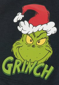 Ilustración del Grinch verde con ojos amarillos, un gorro de Santa rojo y acentos de piel blanca en una camiseta negra, con la palabra "GRINCH" en texto verde.