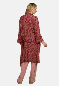 Lange rode bloemenkimono met klokmouwen en een strikceintuur, gedragen over gestreepte broeken. Kenmerkt zich door complexe patronen in beige en groen.