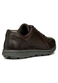 Sneaker in pelle marrone con punta arrotondata, suola in gomma grigia e dettagli texturizzati. Presenta una chiusura con lacci e un tallone rinforzato.